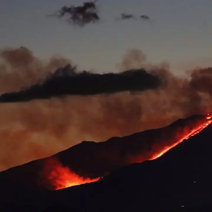 Lo spettacolo dell'Etna in eruzione, dal vulcano lava e un'alta colonna fumo