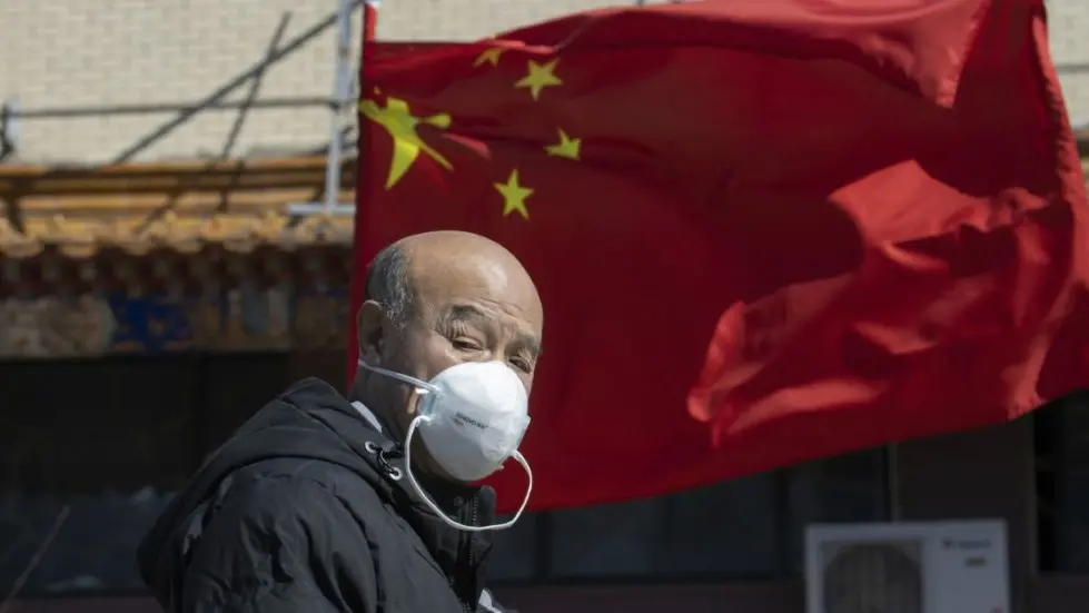 A masked man walks past a national flag outside a traditional medicine hospital in Beijing on Tuesday, March 3, 2020. Mushrooming outbreaks in the Mideast, Europe and South Korea contrasted with optimism in China, where thousands of recovered patients were going home and new virus cases drop to a new low. (AP Photo/Ng Han Guan)