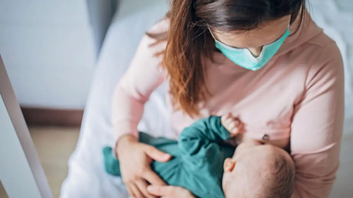 Two people, mother with protective mask breastfeeding her baby son at home, they are at home do to pandemic outbreak quarantine. , Getty Images/iStockphoto
