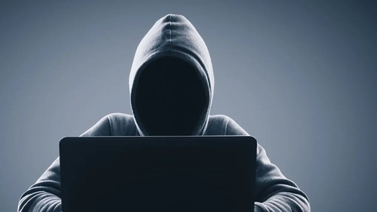 Man with hood using laptop on gray background. Hacker and virus concept. Copy space , peshkov - stock.adobe.com