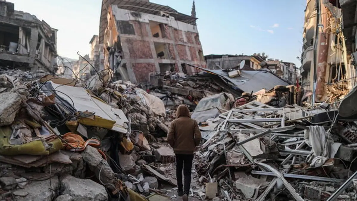 epa10460176 A man walks next to collapsed buildings after a powerful earthquake in Hatay, Turkey, 11 February 2023. More than 24,000 people have died and thousands more are injured after two major earthquakes struck southern Turkey and northern Syria on 06 February. Authorities fear the death toll will keep climbing as rescuers look for survivors across the region. EPA/ERDEM SAHIN , EPA