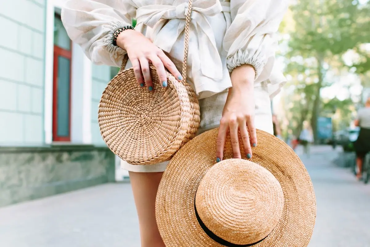 Stylish woman's outfit. Nature stylish top. Straw bag. White dress.Woman hands with fashionable stylish nude rattan bag and straw bag outside. Stylish young woman fashion details