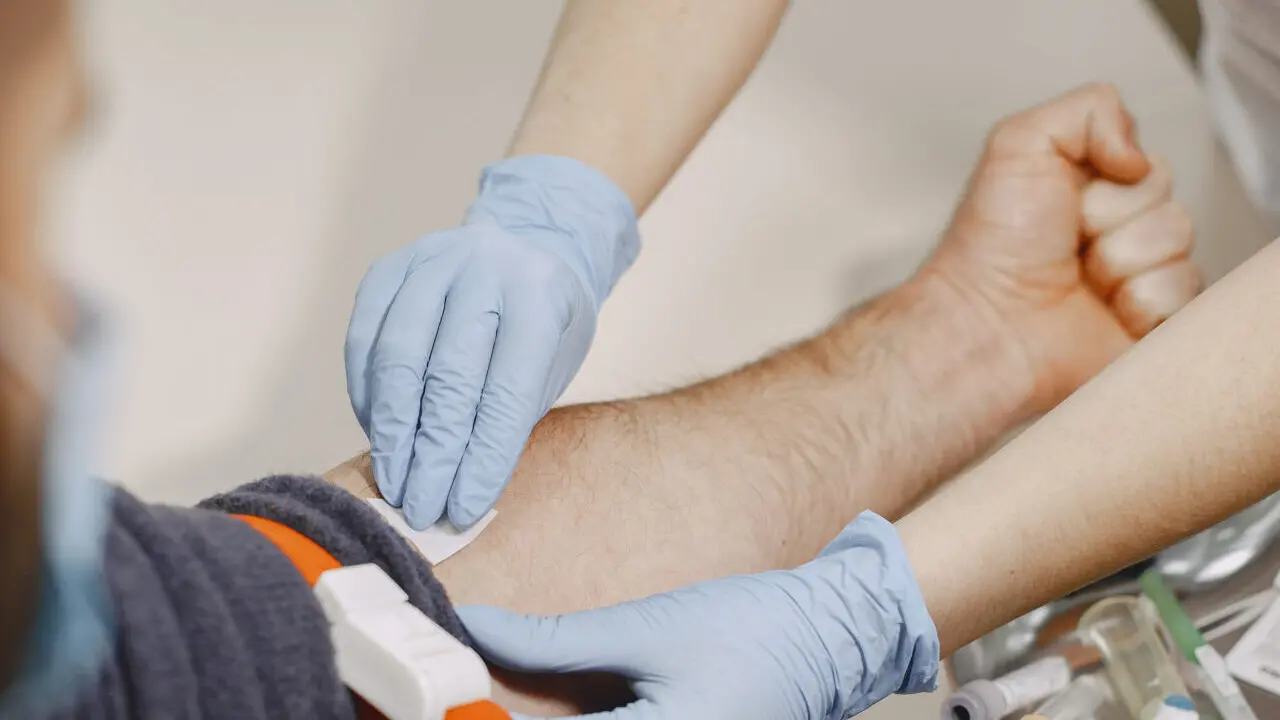 Skillful nurse is doing blood test for man in clinic. Man in a medical mask.