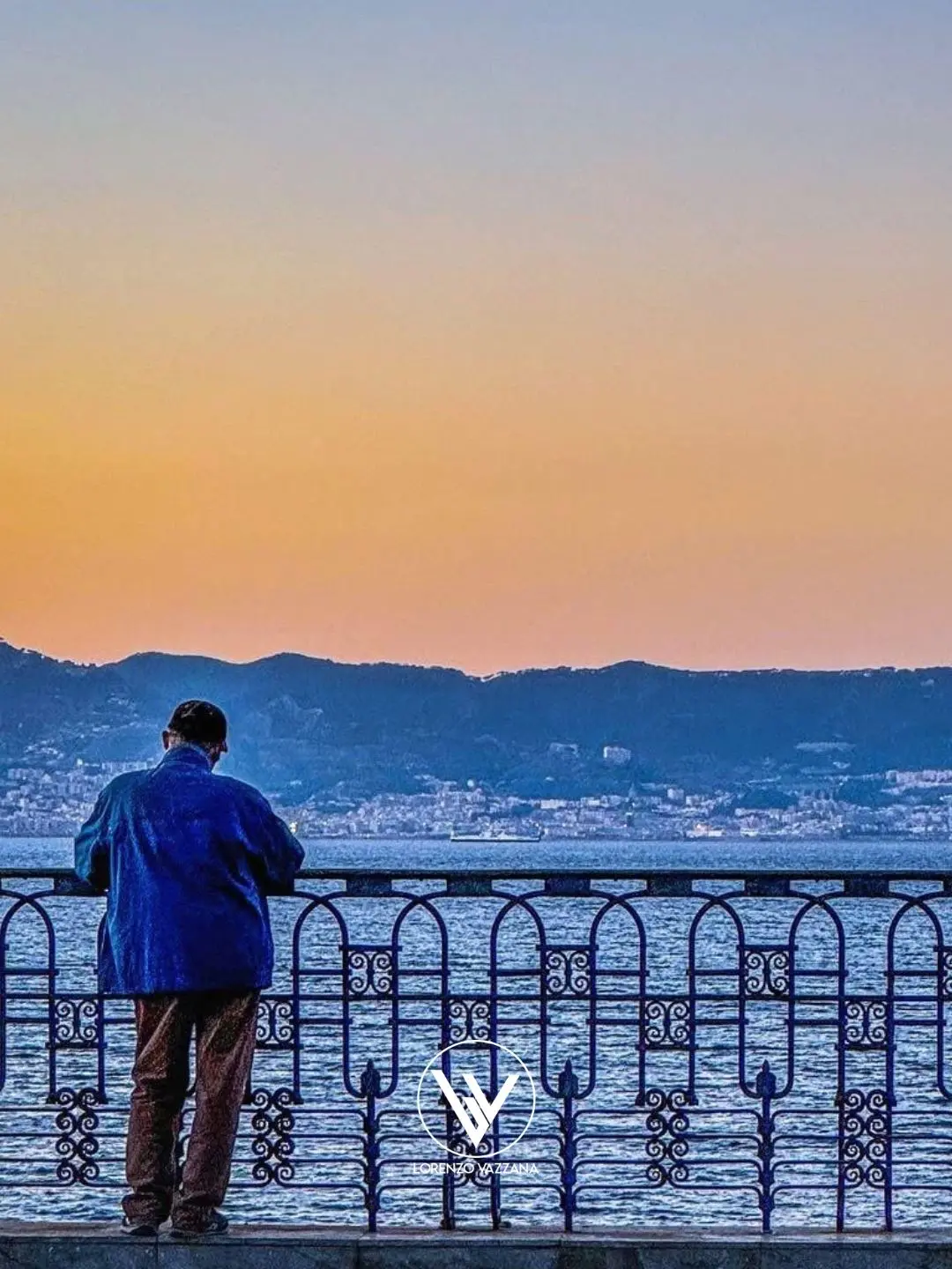 Un uomo solo, affacciato sul lungomare, guarda Messina all’orizzonte avvolta dai colori tenui dell’alba