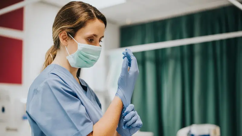 Female nurse with a mask putting on gloves , Shutterstock
