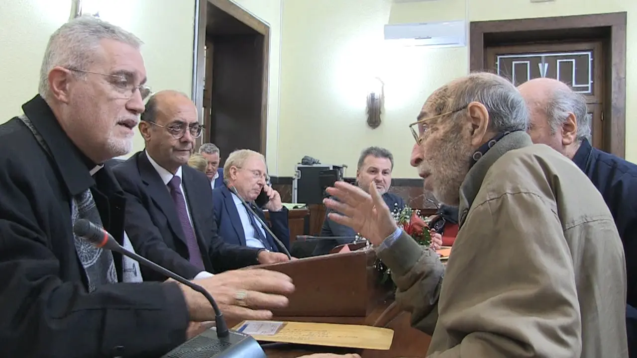 <p>Gerlando Gioffrè mentre parla con il vescovo durante la Conferenza dei sindaci</p>\\n