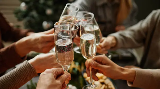Close up of friends clinking champagne glasses while enjoying Christmas dinner together sitting by elegant dining table with candles , Getty Images/iStockphoto