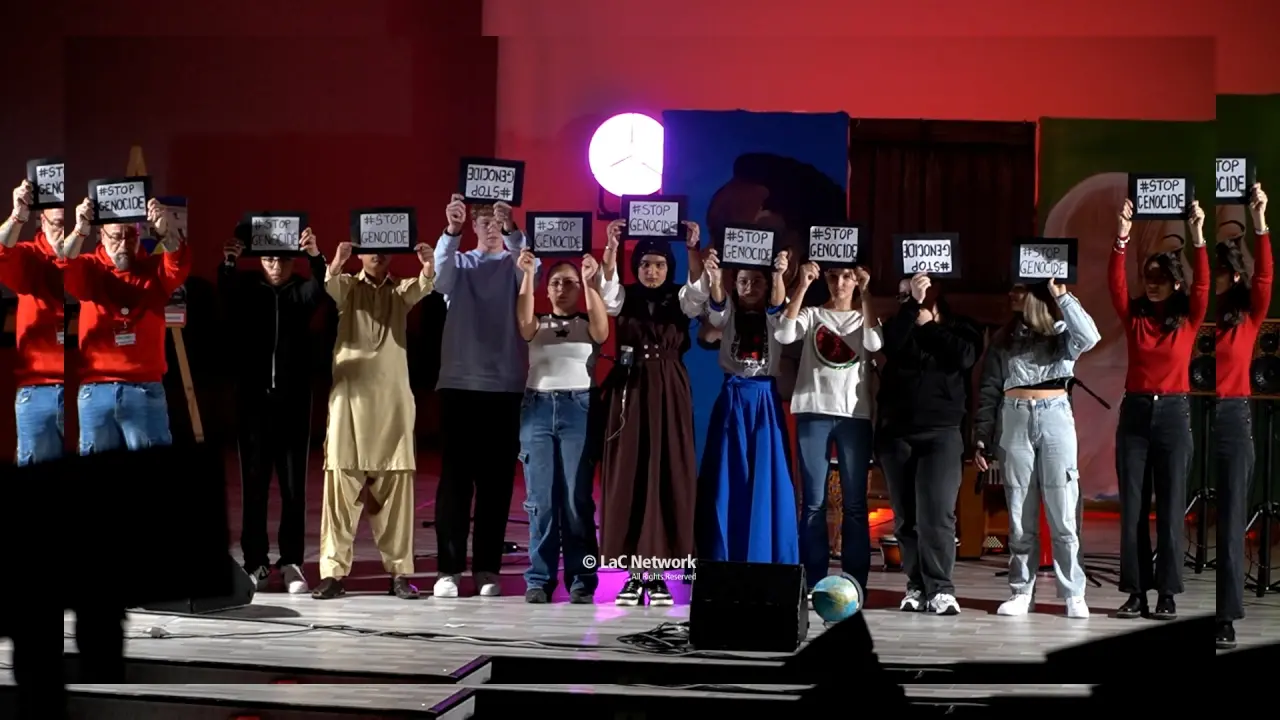 <p>Bambini ed educatori sventolano la scritta "Stop genocide"</p>\\n