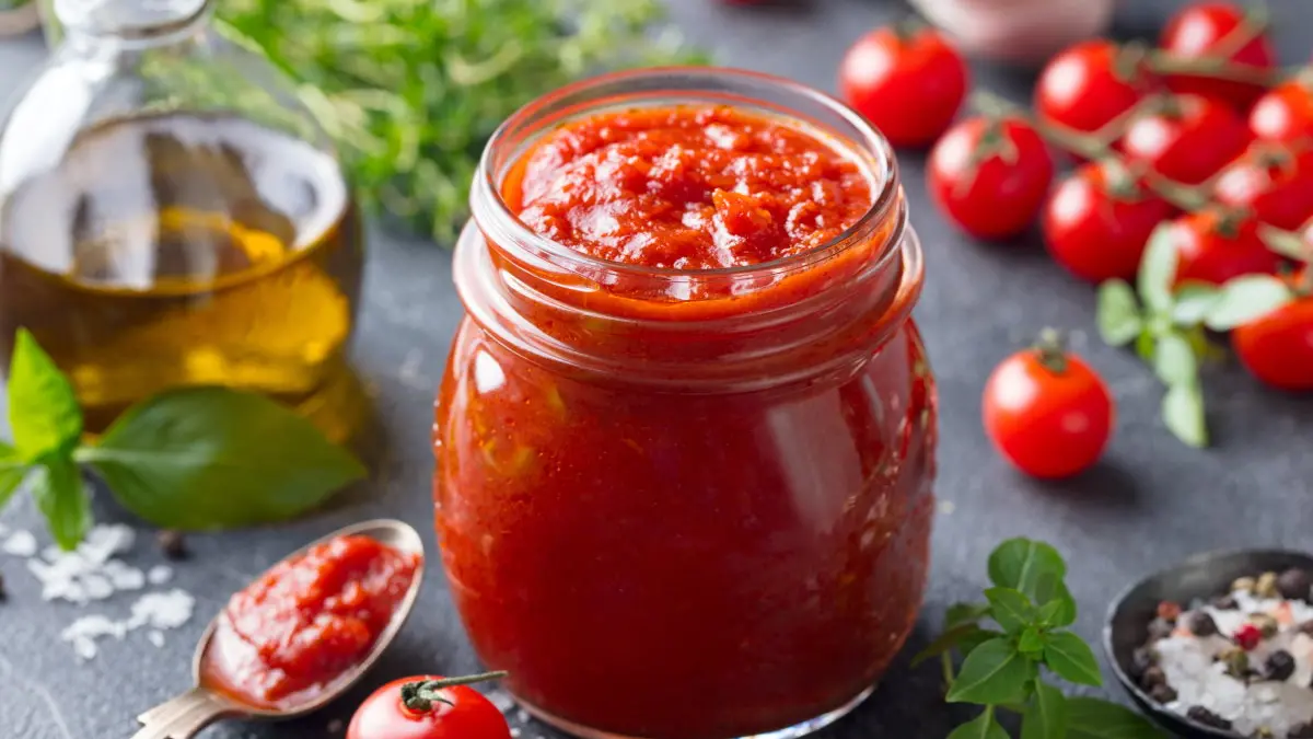 Tomato sauce in a glass jar with fresh herbs, tomatoes and olive oil