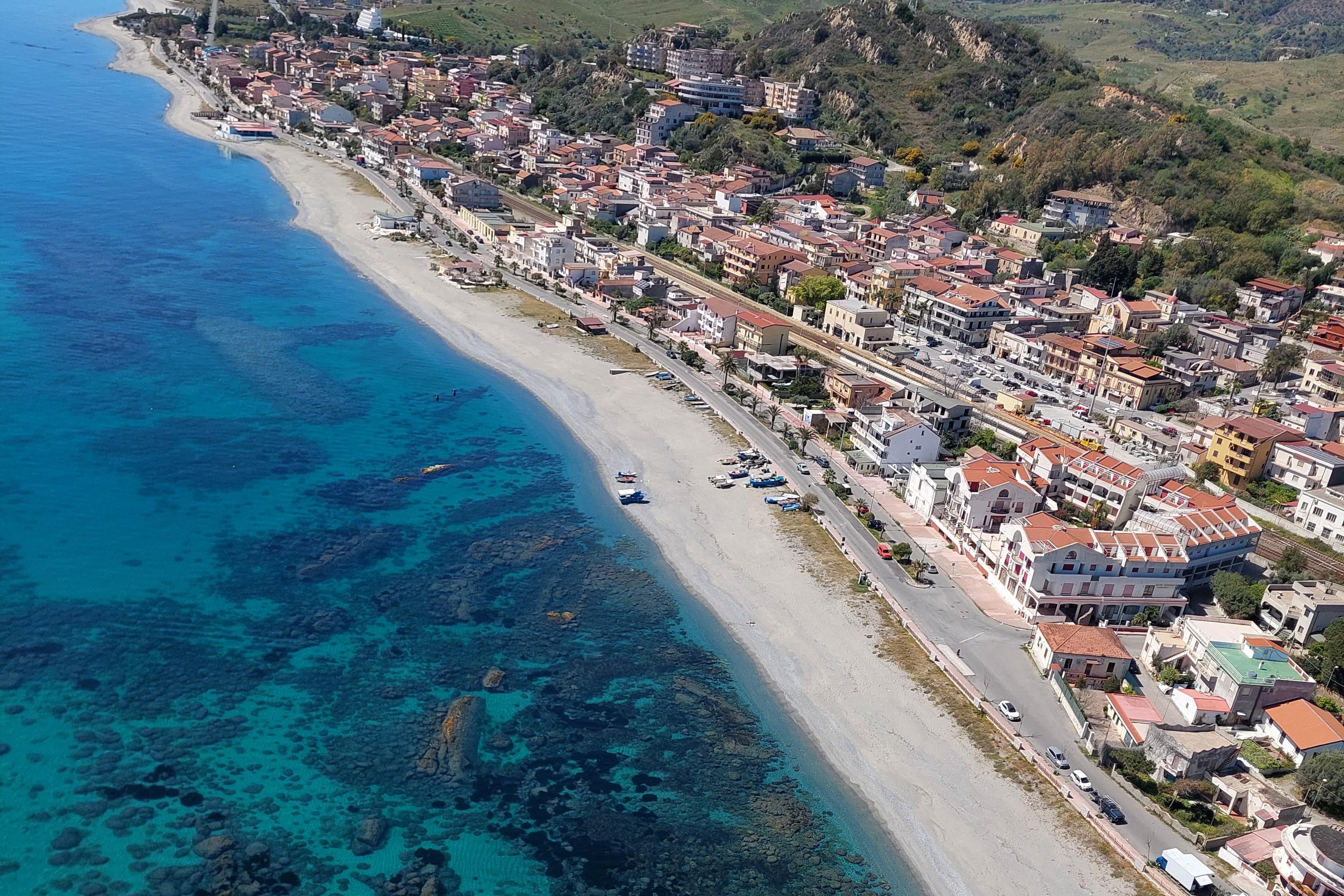 Borgo antico e paesaggi naturali di Brancaleone, con turisti e visitatori in movimento lungo la costa