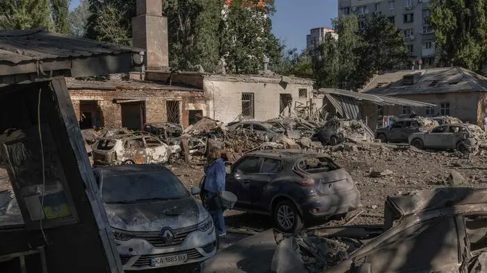 A woman stands next to destroyed cars and damaged buildings following a Russian strike in Kyiv on August 20, 2026, amid Russia\\'s invasion of Ukraine. Russian bombardments killed at least 12 people and wounded dozens in Ukraine\\'s capital and its surrounding region overnight, authorities said on August 20. (Photo by Roman PILIPEY / AFP) , AFP